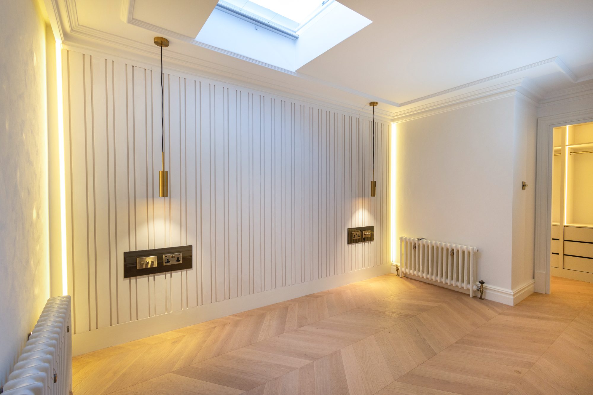 Fluted panelling wall under a skylight with brass pendants and chevron oak floor