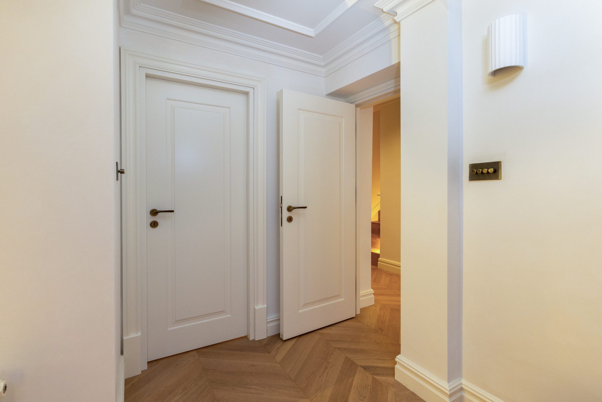 Hallway with panelled doors, brass lever handles and chevron oak floor