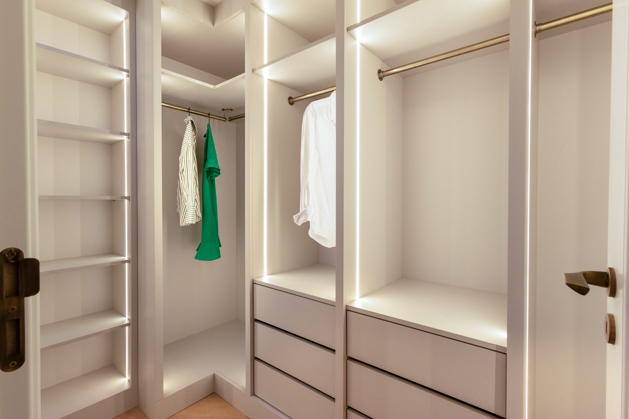 Corner of the walk-in wardrobe with brass hanging rails and drawer banks