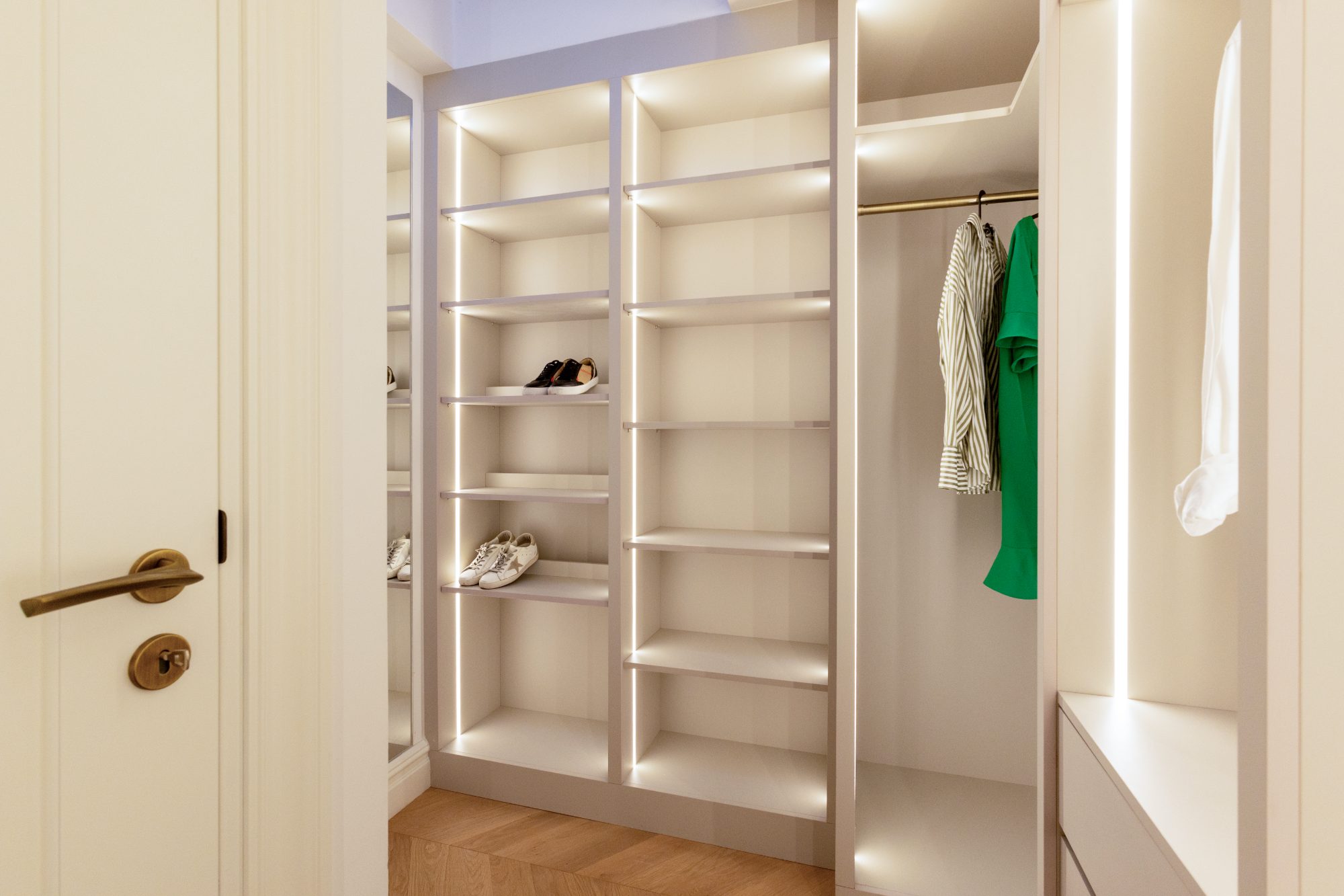 Walk-in wardrobe with lit shelves, brass hanging rail and mirrored return