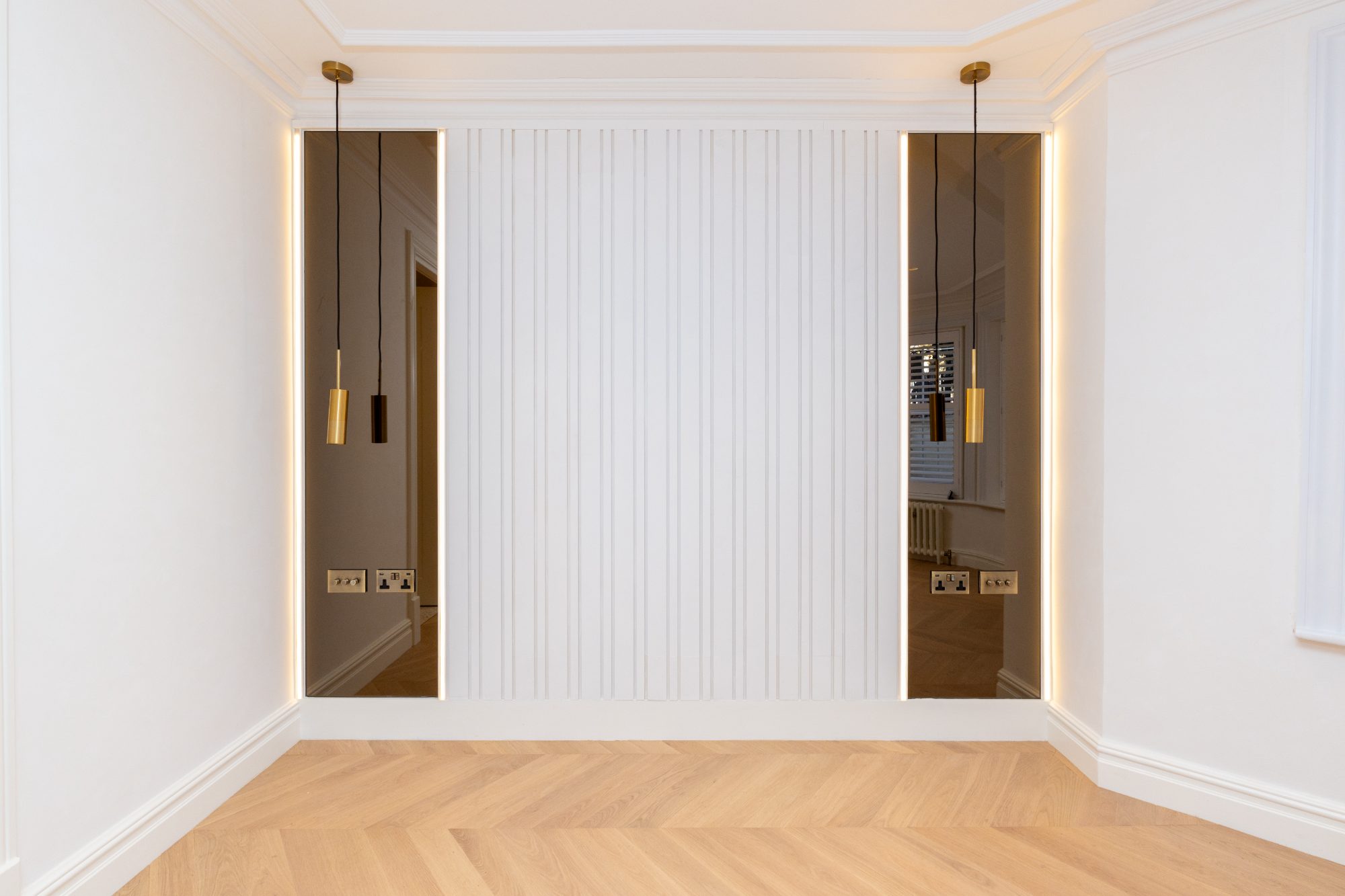 Fluted wall panelling flanked by two backlit full-height bronze mirrors, chevron oak floor